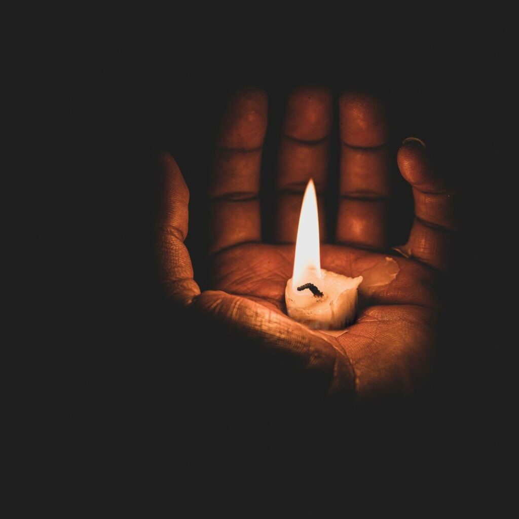 Ein Hand in der Dunelheit mit einer ausgehenden Kerze den Zod symbolsieirend